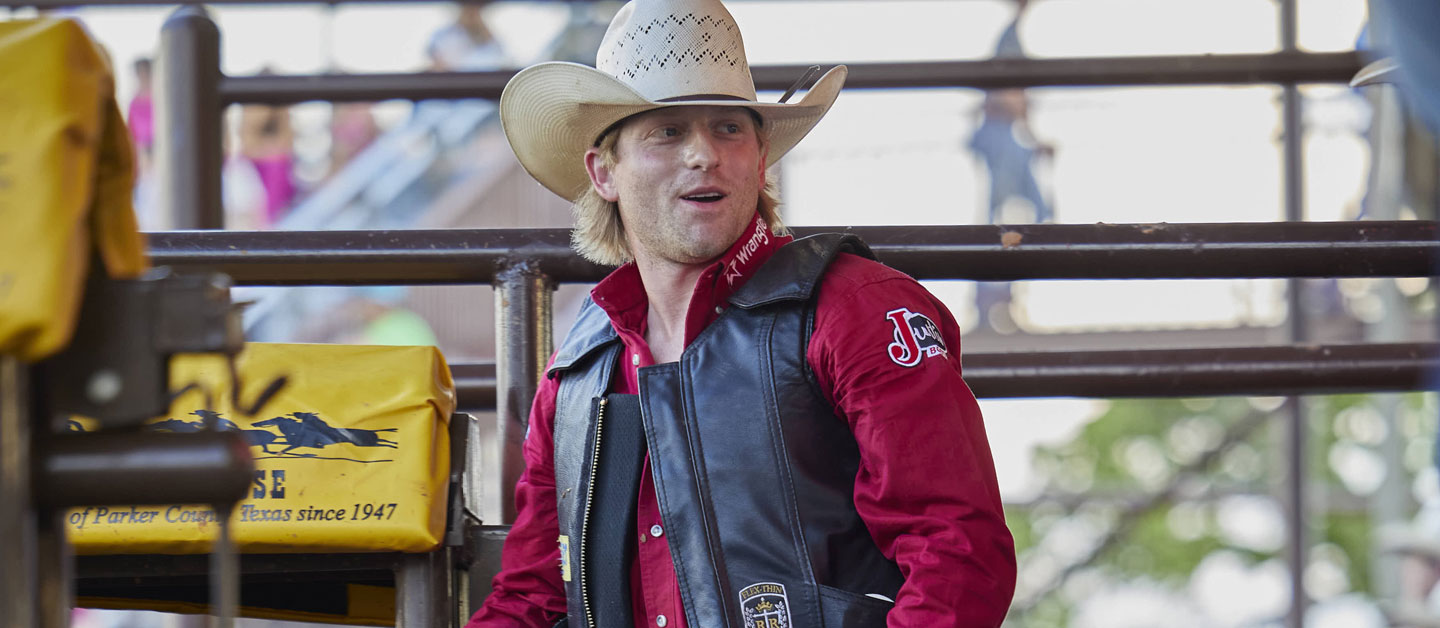 Cowboy wearing a red shirt standing on the chutes looking and talking to someone.